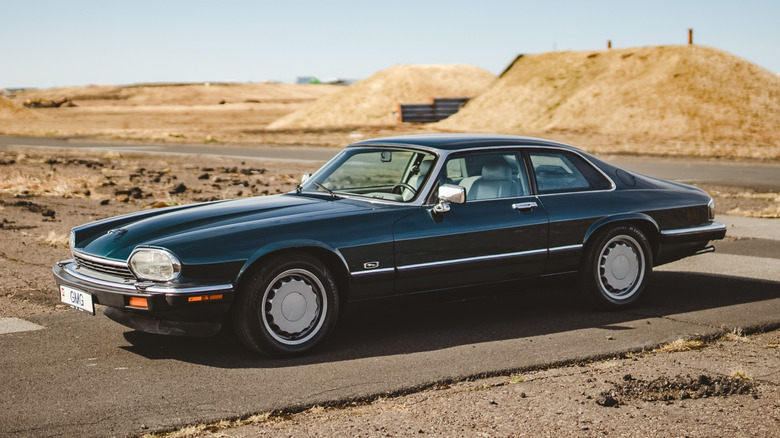 Black Jaguar XJS on a road with small hills in the background.
