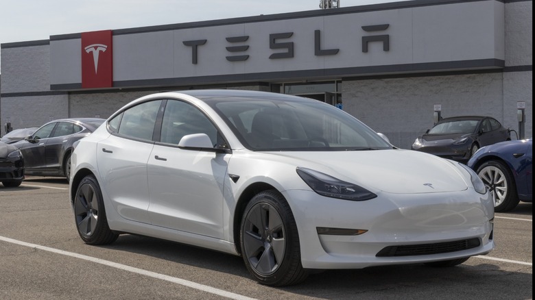 a white Tesla Model 3 parked in front of a Tesla showroom
