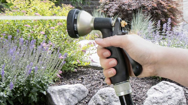Hand holding Orbit 7-Pattern Nozzle attached to water hose