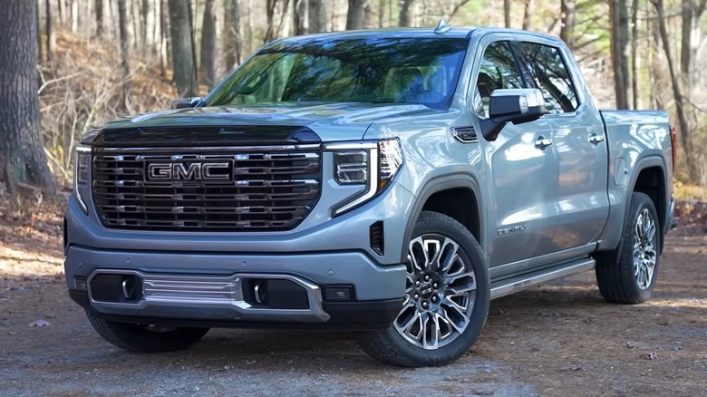 A silver 2026 GMC Sierra 1500 Denali sitting on a dirt path surrounded by bare winter trees.