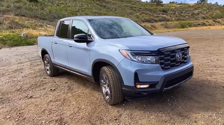 A powder blue Honda Ridgeline sitted on a loose gravel pullout in front of a high desert.