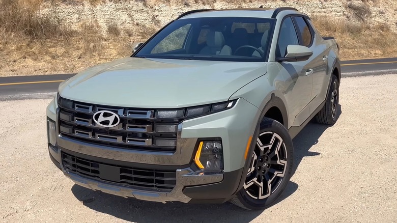 A sage green 2025 Hyundai Santa Cruz parked on the shoulder of a dry desert road with tan hillsides behind it.