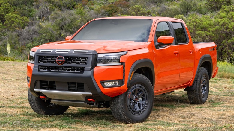A vivid orange 2025 Nissan Frontier Pro-4X truck parked on a dry hillside covered in scrub brush.