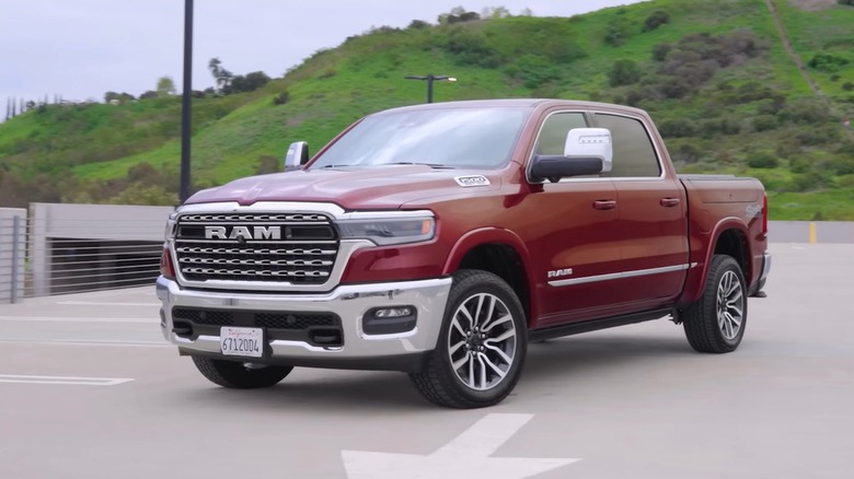 A deep red 2025 Ram 1500 Longhorn crew cab rolling through a rooftop parking structure with green hillsides visible in the background.