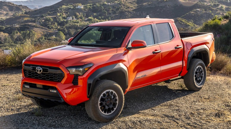 A bright orange 2024 Toyota Tacoma TRD Off-Road Solar Octane crew cab sitted perched on a rocky hillside overlooking a sweeping mountain range.