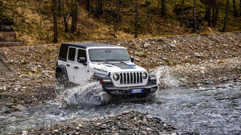 A white Jeep Wrangler Rubicon 2021 fording a shallow creek with water splashing about.