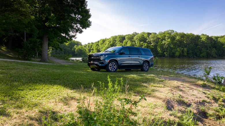 A gloss black 2021 Chevrolet Suburban parked on grass next to a lake.