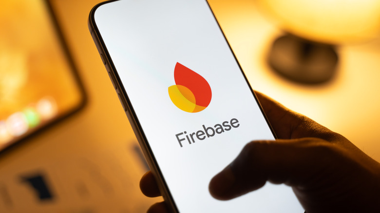 A person's hand holding a smartphone showing the Firebase logo.