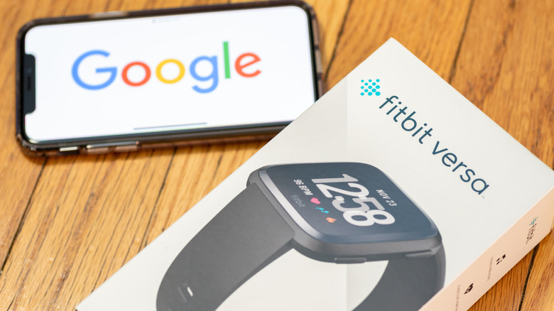 A Fitbit Versa box next to a smartphone showing the Google logo.
