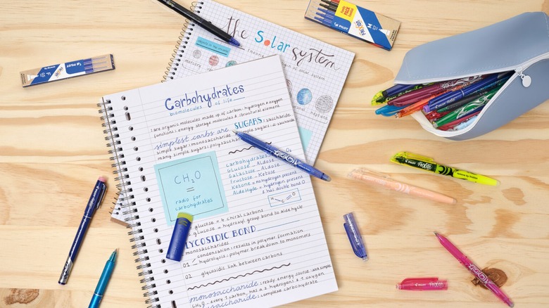Several Frixion Erasable Pens and two notebooks spilled onto a piece of wood