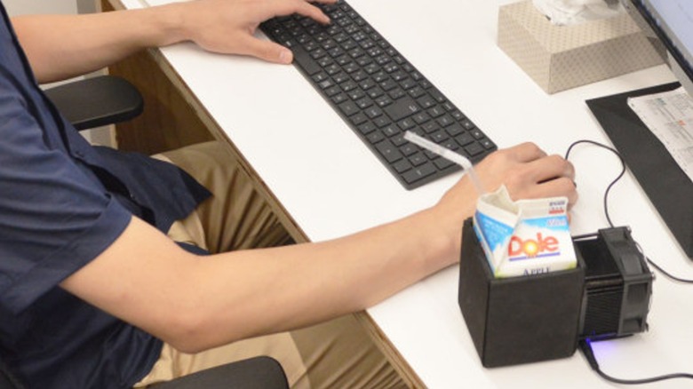 A person working at a desk with the Thanko Super Cold Box for Drinks keeping some juice cool