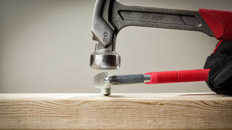 Closeup of a pair of Milwaukee hammers being used on a piece of dimensional lumber