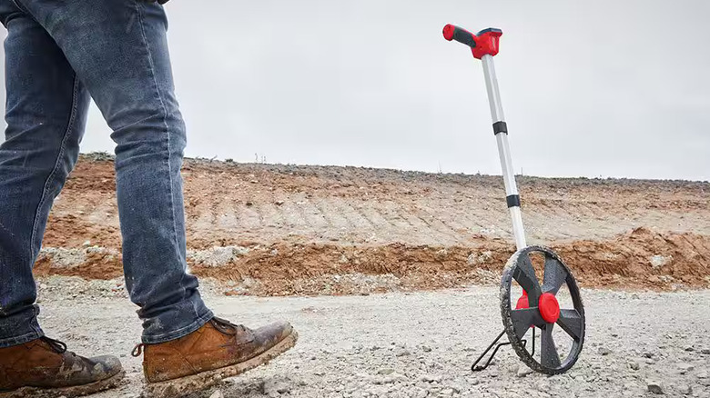 A worker using a Milwaukee measuring wheel on a dirt jobsite