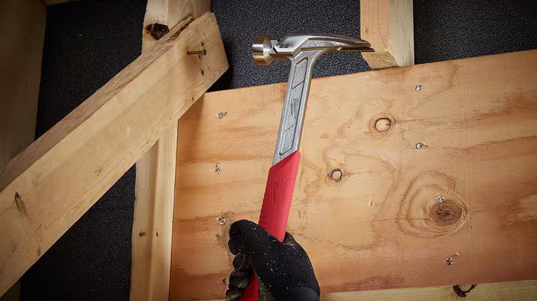 Framer using a Milwaukee hammer to drive a nail into a diagonal 2x4