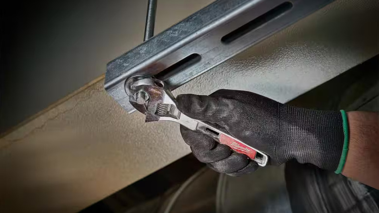 Worker using a Milwaukee adjustable wrench to tighten a bolt on an overhead metal brace