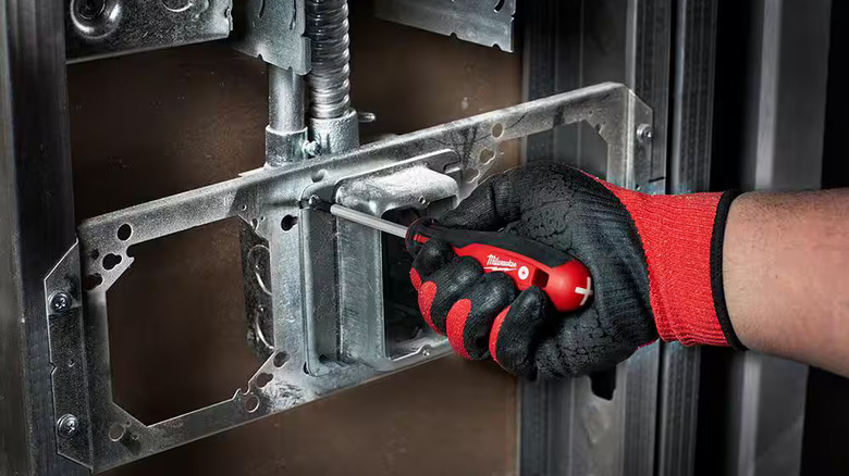 A worker using a Milwaukee screwdriver to tighten a screw on a metal junction box