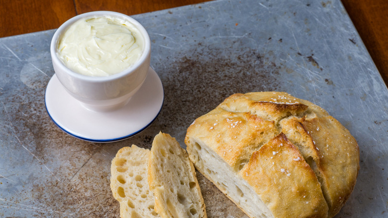 Butter crock next to sliced loaf of bread on a cutting board.