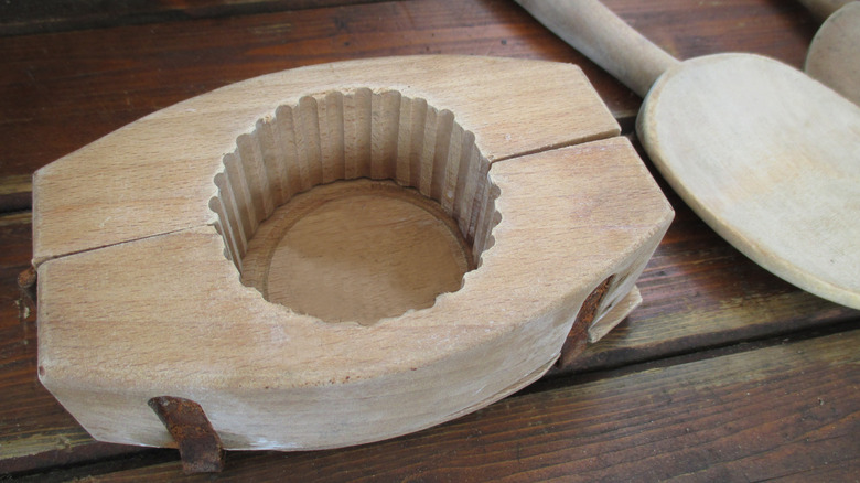 Wooden butter mold with scalloped edges and a matching wood paddle.