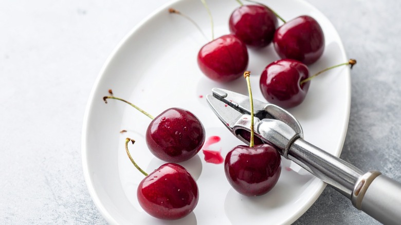 Plate of cherries with a cherry pitting tool.