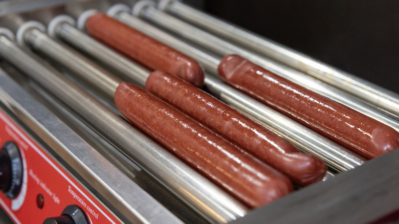 Four hot dot weenies on a rolling hot dog machine.