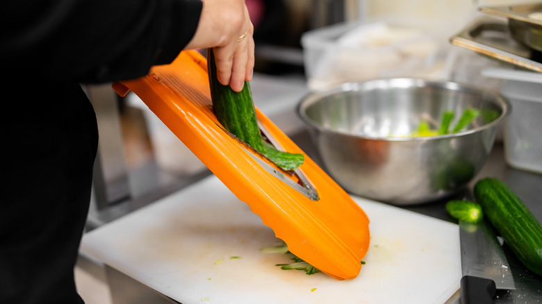 A person using a mandolin slicer to cut a zucchini.