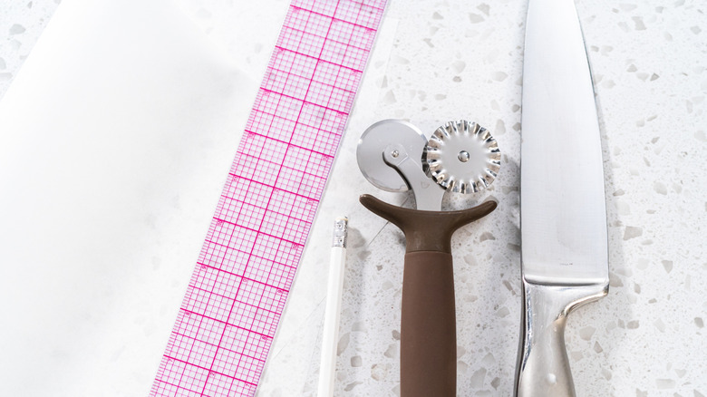 Pastry crimper device in between a knife and a checkered measuring strip.
