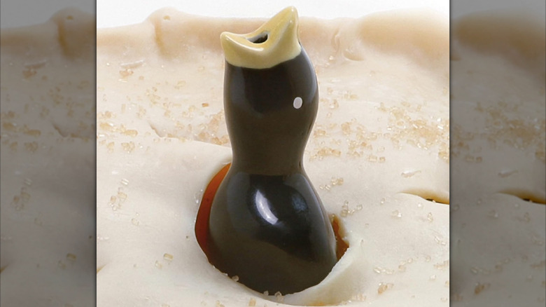 Black ceramic bird with yellow beak inside a pie.