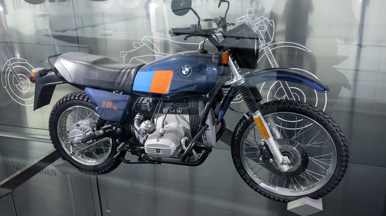 A blue, yellow, and black BMW R80 G/S adventure bike on display on a stage indoors.