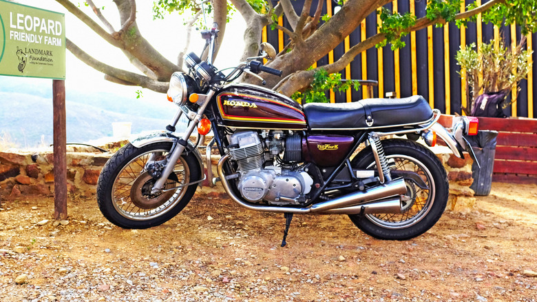 A black and gold Honda CB750 classic bike from 1976 parked under a tree.