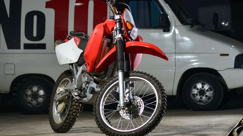 A vintage red and white Honda XR650R bike parked in a garage with a white van in the back
