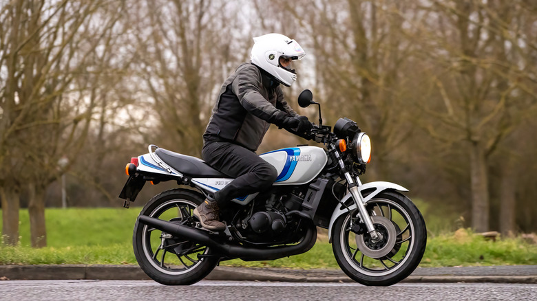 A gray and blue Vintage Yamaha RD350 bike being ridden by a rider in full gear.