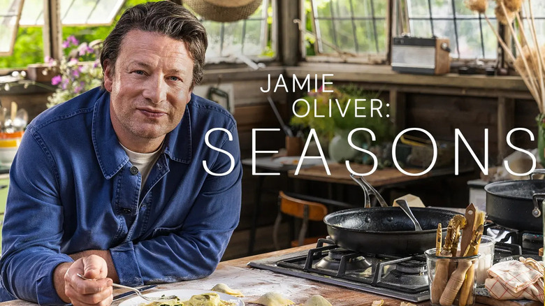 Jamie Oliver eating a dish in a green room kitchen.