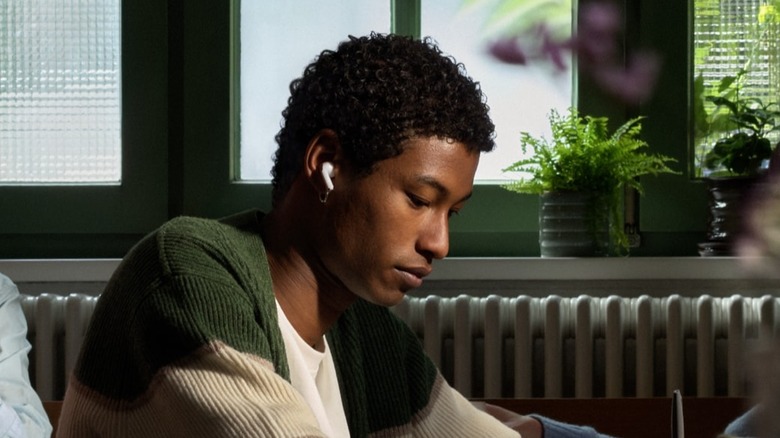 A person sitting at a table in public wearing the Apple AirPods .