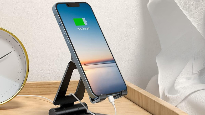 An iPhone tucked into a Nulaxy cell phone stand and charging on a nightstand.