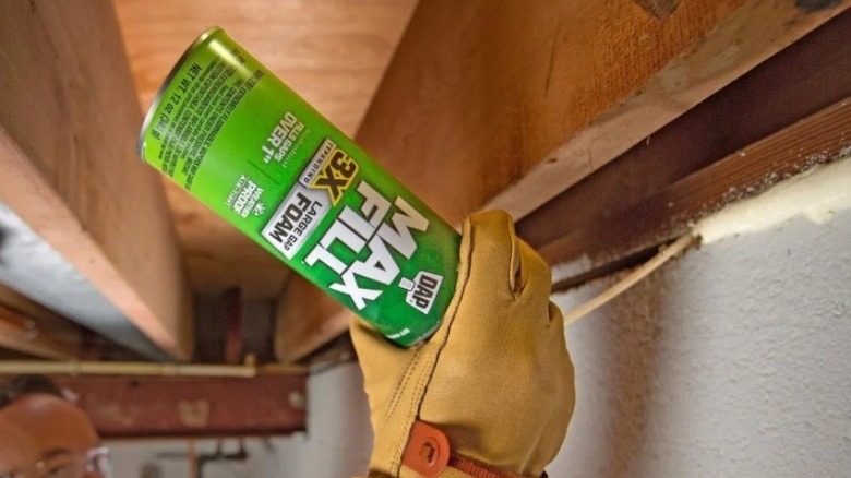 Hand using a can of foam seal to fill gaps near a ceiling