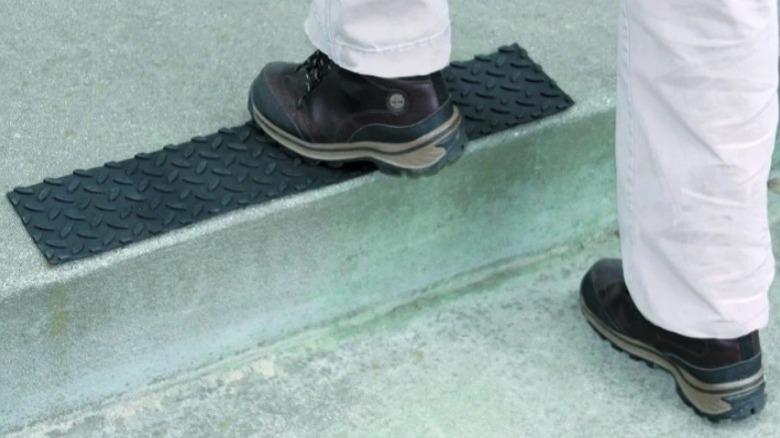 Pair of feet in boots with the left foot stepping up onto a black mat