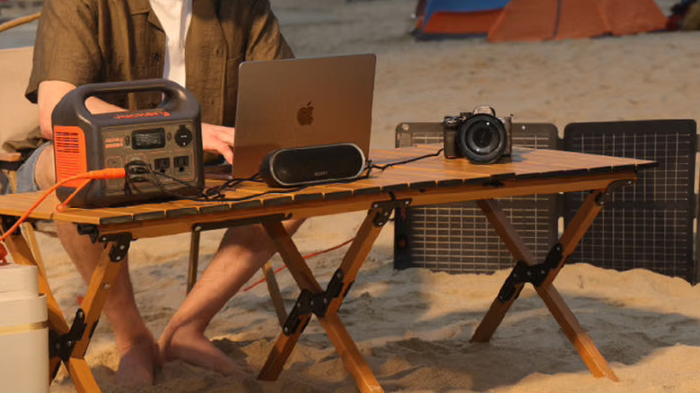 A Jackery Explorer on a wooden table at a beach, powering multiple devices
