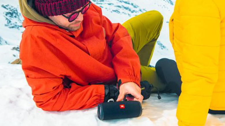 JBL Flip 5 speaker being used outdoors in the snow by a couple on the side of a mountain
