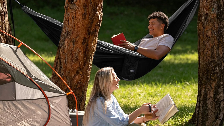 Kootek hammock held up by a pair of trees in the background of a camping site