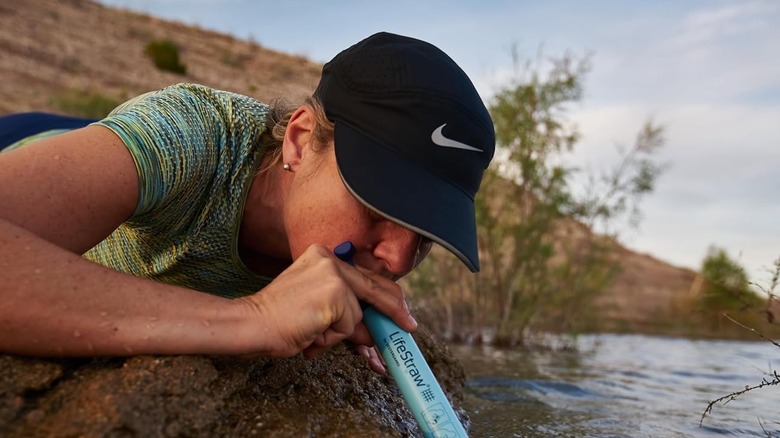 Woman lying on a rock as she uses the LifeStraw by drinking from a river