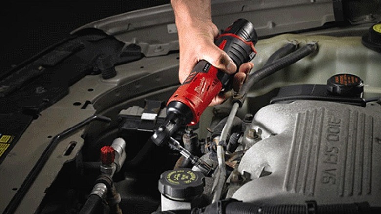Using a Milwaukee ratchet to work in a vehicle's engine.