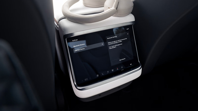A pair of white headphones resting atop the center console screen of the 2026 Tesla Model S, as seen from the second row of seats