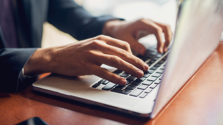 A person typing on a laptop keyboard in a bright room