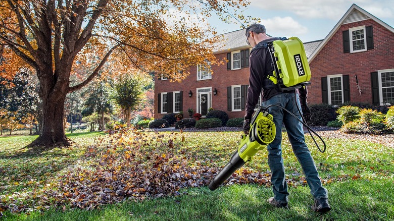 Man using a Ryobi backpack power supply while doing yard work