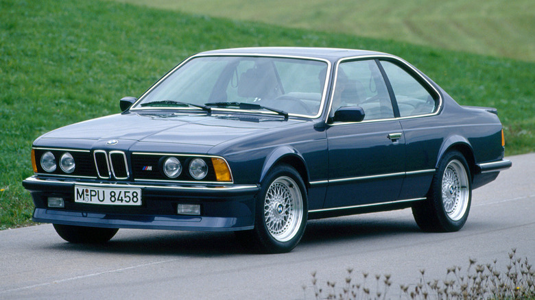 A dark blue BMW E24 6 Series on a road near grass.