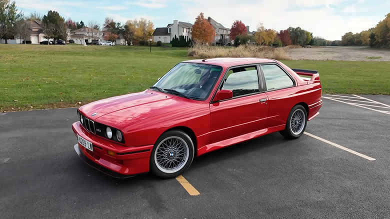 A red BMW M3 E30 parked near a lawn.