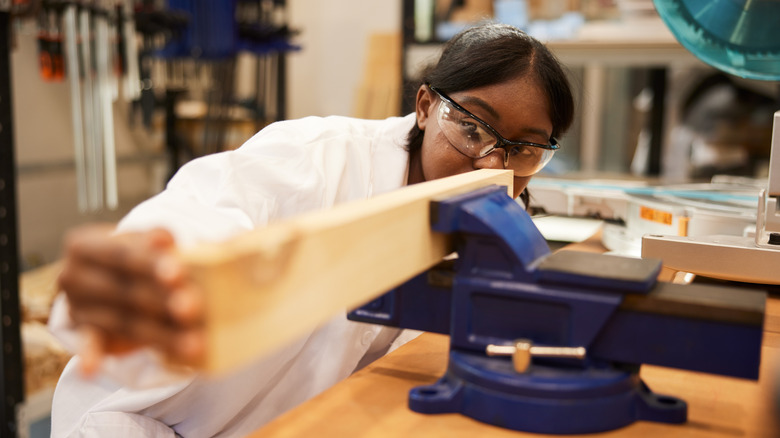 A person holding a wooden plank in a vice clamp