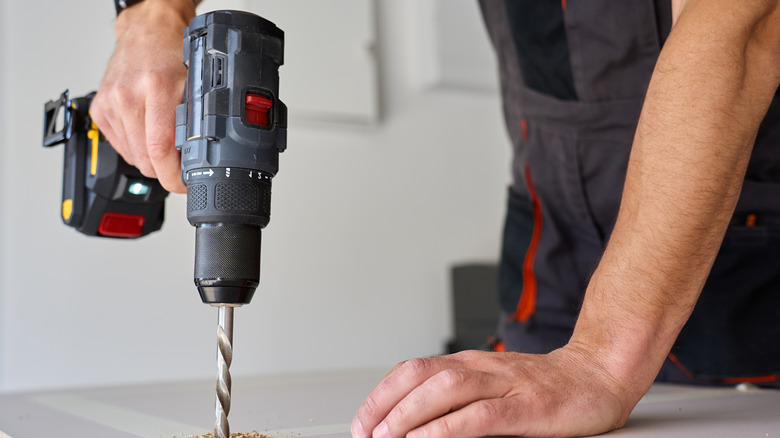 A person drilling a hole in wood with a cordless drill