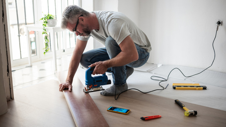 Man using a tool to install a piece of flooring
