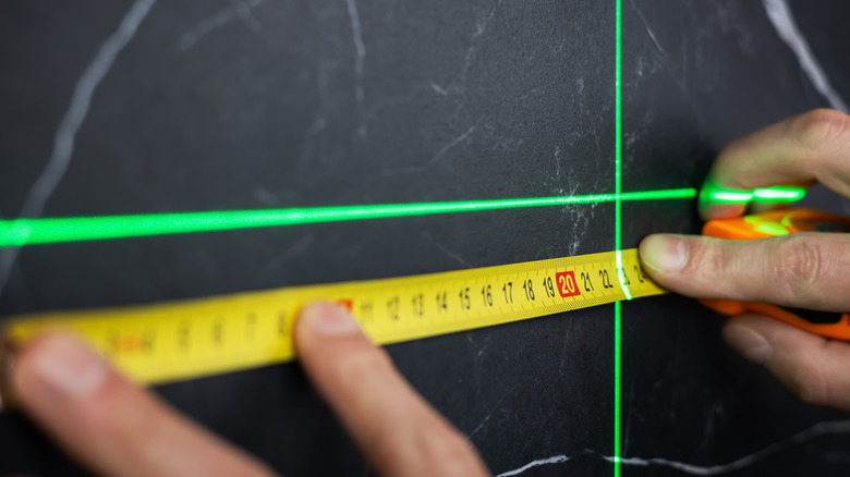 Hand using laser beam and tape measure against a black surface